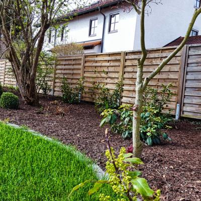 Ein Garten mit Grünfläche und Pflanzenbeet, dass mit frischem Rindenmulch versehen wurde.