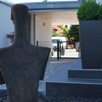 Ein Eingangsbereich mit Statue und Pflanzenkübel mit Buchsbaum vor der Haustüre.