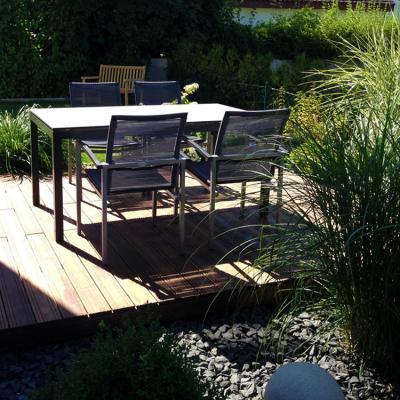 Eine Holzterrasse mit Gartenmöbel auf einem Kiesbeet. In dem Kiesbeet wächst Chinaschilf.