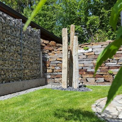 Drei Steinsäule (ca. 3 m) aus Basalt (Naturstein) dienen im Garten, vor einer Steinmauer, als Blickfang.