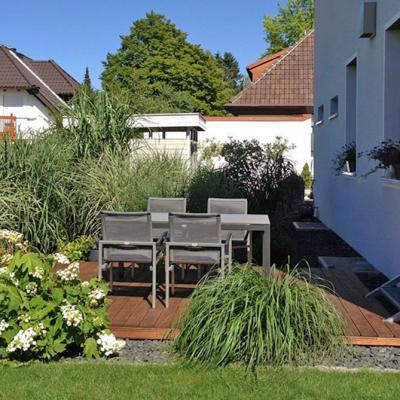 Eine Terrasse aus Holz mit dunkler Gartengarnitur. Verschiedene Grünpflanzen schmücken am Rand die Terrasse.