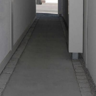 Ein überdachter gepflasterter Gehweg zwischen Haus und Garage.