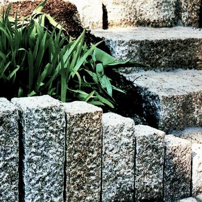 Ein bepflanzter Steinrand aus Granit. Dahinter eine zweistufige Steintreppe.