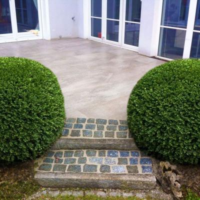 Terrasse aus Feinsteinzeug und Mosaik Treppe. Auf beiden Seiten der Treppe sind jeweils ein großer Buchsbaum.