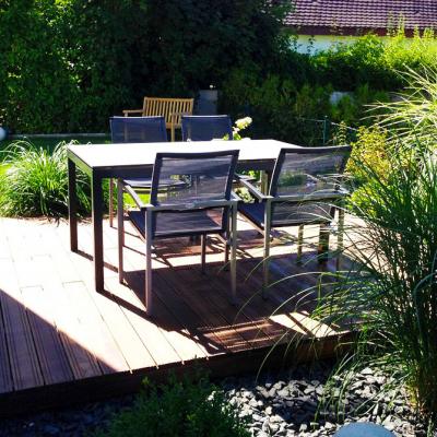 Eine Terrasse aus Holz auf Kiesbeet. Umgeben von Chinaschilf und anderen Pflanzen.