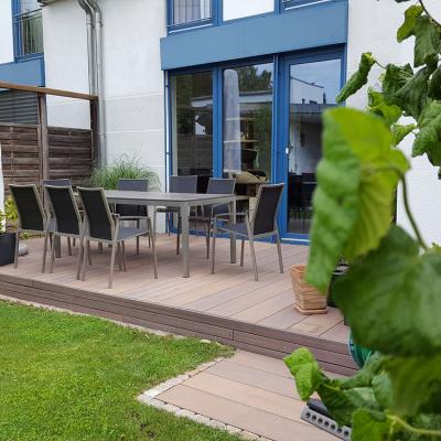 Terrasse mit Holz-Lamellen. Am Rand sind kleine Mosaik-Pflastersteine verlegt.