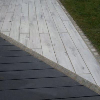 Terrasse mit Paneelen in unterschiedlichen Farbflächen. Eine Reihe Pflastersteinen durchtrennt beide Flächen.